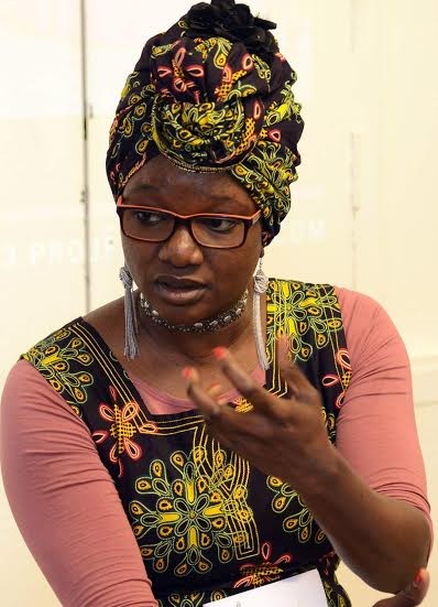 Une femme noire à foulard et lunettes explique.
C'est Ndella Paye.