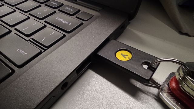 The photo shows a YubiKey 5 inserted into a laptop's USB port. The YubiKey (U2F key) is attached to a keyring.