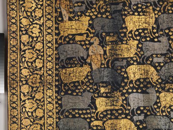 closeup of the textile design showing the ornamental border and primary design of a herder surrounded by gold and silver cows