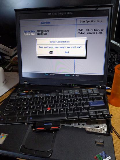 An IBM ThinkPad T43 laptop in partial dissemblily, in the BIOS awaiting confirmation to save configuration after updating the date & time