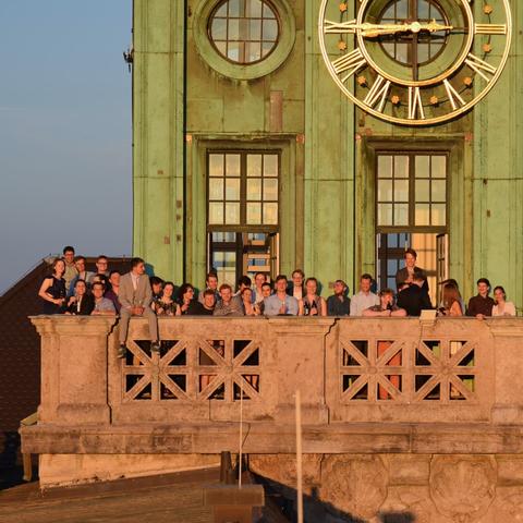 Members of our student club are standing on the balcony of the clock tower during sunset
