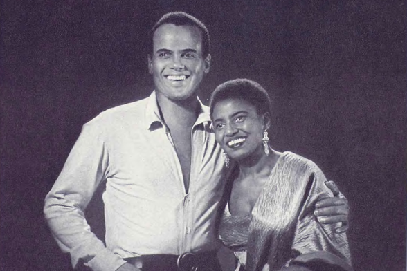 1965 Two people standing close to each other, smiling and looking at the camera.

"A man and a woman in front of a microphone, both appear to be happy and relaxed."
Tags: "two people", "microphone", "happy", "relaxed", "man and woman"