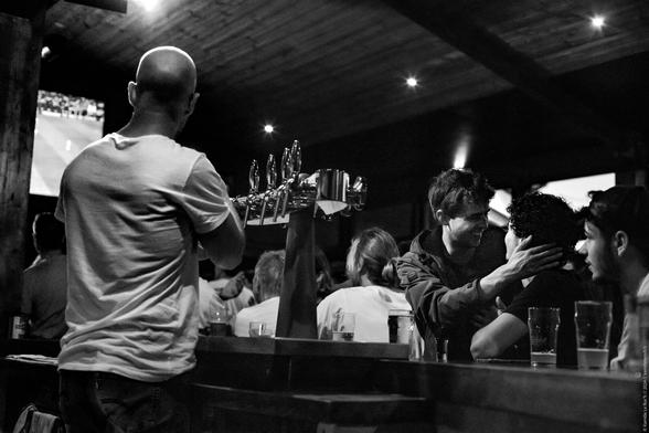 Photo en noir et blanc contrastée. Nous sommes dans un bar- pub breton, sur le mur un match de foot passe à la télé, l'auditoire est captif et la barman est en train de servir une bière à la tireuse, mais sur la droite, deux personnes ignorent totalement l'enjeu du match et s'apprêtent à s'enlacer joyeusement