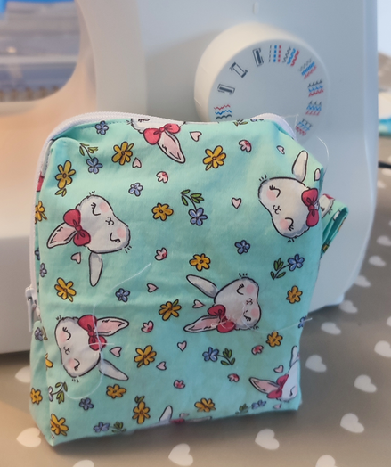 Small pouch, hand made. Fabric patter is some cute bunny heads with a ribbon on one of the ears. There are flowers and hearts between.