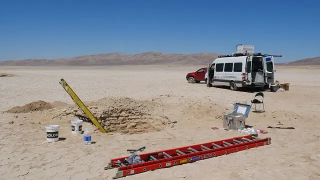 research site in a desert with cars, ladders, and a hole in the ground