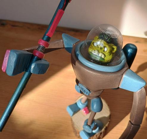 A close up of the face with helmet and clamplike hands. It has large nostrils prominent teeth and dark green lips.