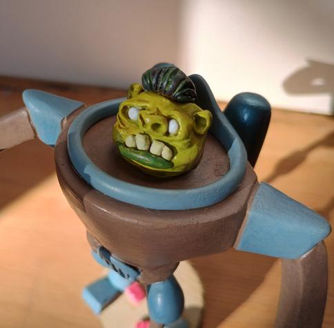 A close up of the face without the helmet. You can see it's grimacing face and little black pompadour haircut.
