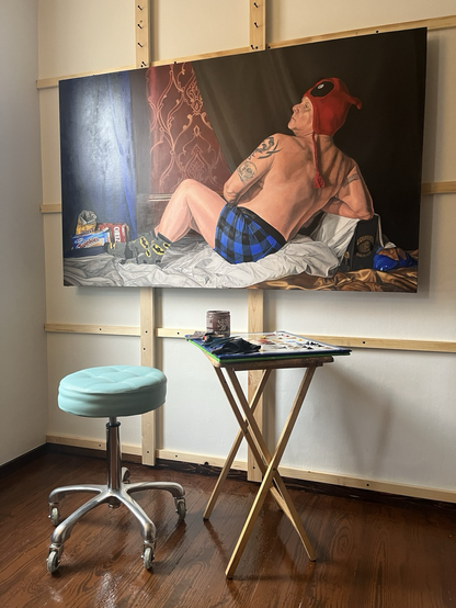 A roller stool and a painting palette stand on the wooden floor in front of a partially-complete painting of a partially dressed dude.