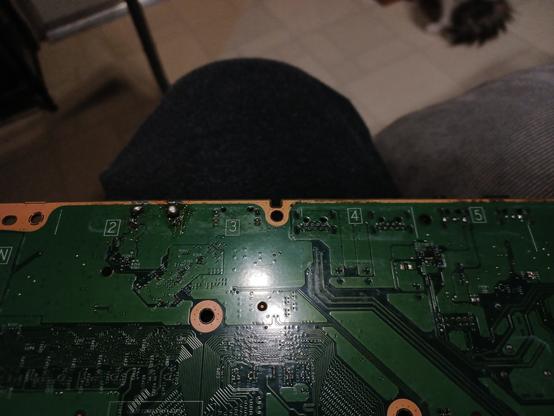 bottom of an Xbox One S motherboard, sitting on my leg. even with the big flash spot in the middle of the pic, you can see to the left of it 2 huge solder blobs where someone failed to properly replace the HDMI out port.