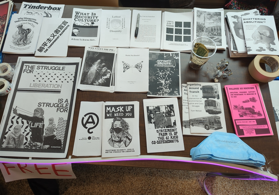 A table with zines on security culture, DIY estrogen, police and prison abolition, a statement from some of the Stop Cop City RICO defendants, Affinity Groups, and more