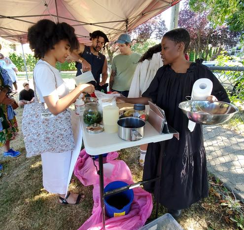 Instructors & workshop attendees, working on mixing indigo & hibiscus photo developing fluids, on a table under event tent, in the park.