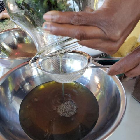 Straining infused indigo water into a stainless steel mixing bowl.
