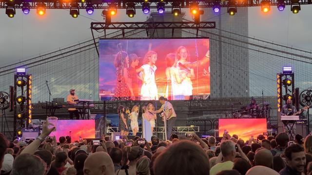 A view of Michael Franti at The Rooftop at Pier 17 in NYC at the Michael Franti & Spearhead show on Friday July 12, 2024. He is on stage with some children he brought up to sing with him and is holding the microphone for a young person who is singing.