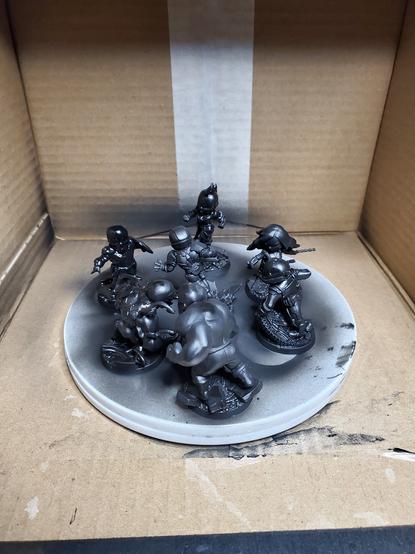 Black primed Marvel hero minis on a formerly white lazy susan inside a cardboard box.