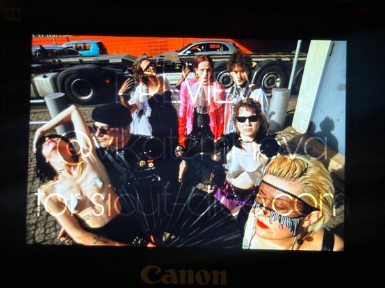 Same 7 people standing next to a road with heavy traffic. Sicut is leaning back on Heinzel, July is having her fan open and eyes closed, Gene is dancing, everyone else is just looking pissed. All dressed up in lace, latex, leather, glitter and uniform