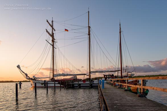 DE: 
Das Bild zeigt das Segelschiff "Weisse Düne" im abendlichen Sonnenuntergang vor dem Seesteg in Neppermin im Achterwasser des Peenestrom auf Usedom. Details zum Schiff: https://www.weisse-duene.com/schiff.html

EN:
The picture shows the sailing ship "Weisse Düne" in the evening sunset in front of the jetty in Neppermin in the Peenestrom on Usedom. Details about the ship: https://www.weisse-duene.com/schiff.html