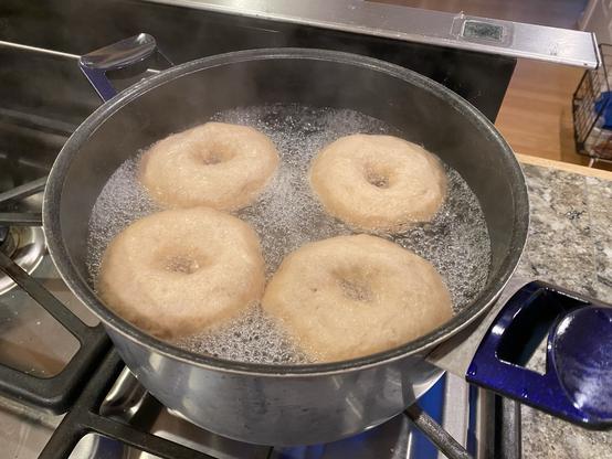 four bagels in a big pot of boiling water on a stove, bubbling away
