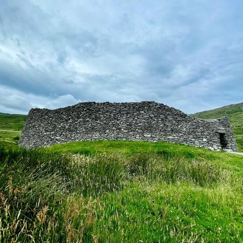 Ancient stone structure in a grassy field under a cloudy sky.