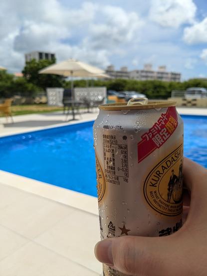 A can of beer held up in front of a pool