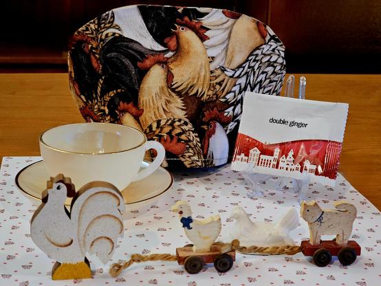 A tea tableau of a crowing rooster loudly & proudly exhibiting himself while a trail of little guys (duck, chicken, cat) on wheeled platforms are pulled behind him with fraying rope. The tea is Double Ginger from Adagio Teas.