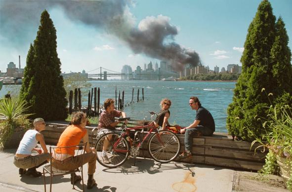 Five white people lounging on a gentrified stretch of Brooklyn waterfront, seemingly oblivious, as the World Trade Center towers burn in the distance on Sept. 11, 2001. Photo by Thomas Hoepker.