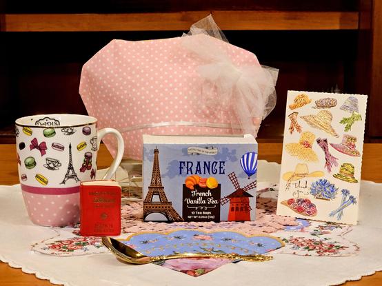 A vivacious tea tableau in happy pastel colors with recognizably French/Parisian details like high fashion, the Eiffel Tower, macarons, fancy bows, a hot air balloon, ladies' fans, pink polka dots, and French Vanilla black tea... all of this to celebrate France's holding of the line against extremism, and a wish that we all might yet do so.