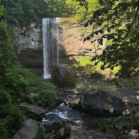 Hemlock Falls in Georgia's Cloudland Canyon. A broken stream of water drops over the top of a thick rock ledge. To the right of the waterfall the sun highlights an orangish section of the ledge. The left is in shadow and the rock seems white. A pool at the base of the falls empties into a stream near the viewer's position.