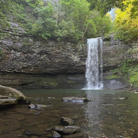 Cherokee Falls, also in Georgia's Cloudland Canyon. A larger stream falls over another thick rock ledge into a large pool at the base. The rock face is grey with white sections. Trees in various shades of green surround the top of the falls.