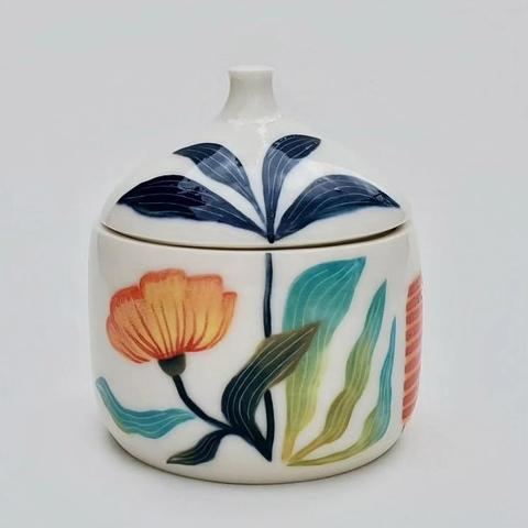 Vue d'un côté de la boite en porcelaine. Une grande fleur deploie des feuille jusque sur le couvercle