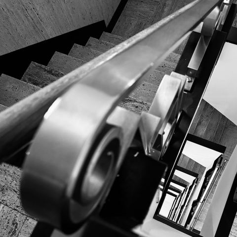 Looking down over the railing into a straight geometrical staircase with an circular Art Deco handrail.
