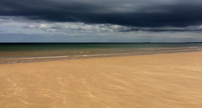 The photographer was stood in the blazing sunshine on a sandy beach looking out to sea as dark storm clouds gathered overhead.