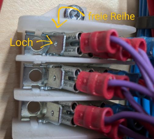 Foto eines an Holz angeschraubten Blocks mit mehreren orthogonal herausragenden Flachsteckerzungen nebeneinander. Eine Reihe Zungen ist unbelegt, so dass man die Löcher darin gut erkennen kann.