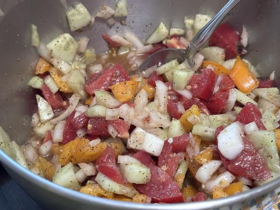 A bowl of vegetable salad with chopped tomatoes, cucumbers, onions, and yellow bell peppers, seasoned with herbs and spices.