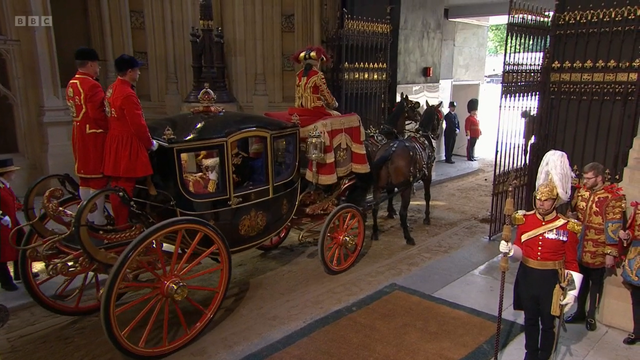 Hovin jäsenten hevosvaunut ovat lähdössä Westministeristä, rakennuksen sisältä. Vaunut ovat koristeelliset ja mustat, pyörissään punaista, niiden edessä on kaksi mustaa hevosta vetämässä. Ajopukilla on punakultainen suuri kangas, ja ajaja on pukeutunut punakultaiseen prameaan asuun. 

Vaunun perässä, sen ulkopuolella, takapyörien kohdalla seisoo kaksi vähän vaatimattomammassa punakultaisessa asussa olevaa miestä.