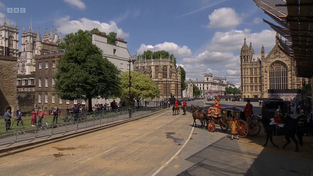 Vaunu on ajanut ulos Westministeristä, sen edessä jonkin matkan päässä on kaksi punatakkista ratsastajaa. Taustalla näkyy Westiminsterin tienoon vanhoja, koristeellisia rakennuksia, vähän puita, ja ihmisiä, jotka seuraavat ja kuvaavat tapahtumia. Päivä on aurinkoinen, sinitaivaalla joitain valkeita pilviä.