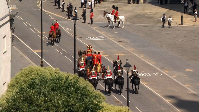 Hovin jäsenten kuninkaallisia koruja kuljettava kulkue on päässyt aloittamaan matkaansa. Vaunujen edessä jonkin matkan päässä edelleen kaksi puna-asuista ratsastajaa´,

Vaunujen takana U-muodostelmassa kuusi ratsastajaa. 

Kadulla näkyy muutamia poliiseja sekä muutama niitä mustissa karhunkarvahatuissaan ja punaisissa takeissaan olevia tyyppejä.