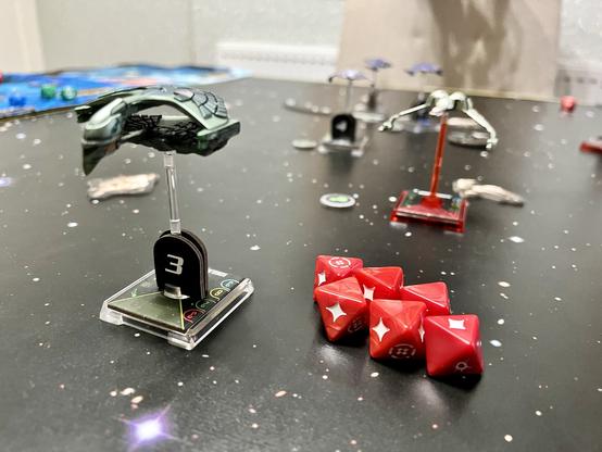 Star Trek Attack Wing in play. Romulan bird of oret in the foreground. A Klingon K’vort bird of prey not far behind. Six red attack dice clearly visible.