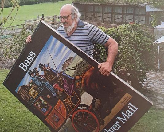 Man carrying a large painted pub sign in a rural setting.