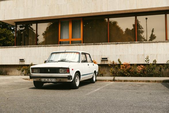 The image shows an older model car parked in what appears to be a public parking space. The vehicle has a distinctive boxy shape, which is characteristic of some cars from the 1970s or
1980s. There's no visible text on the car or nearby buildings to provide context about its make or model. The setting looks like an urban environment with concrete surfaces and what might be
part of a sidewalk or walkway.