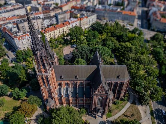 Aerial view of a Gothic-style church surrounded by trees and residential buildings in a city.

Widok z lotu ptaka na gotycki kościół otoczony drzewami i budynkami mieszkalnymi w mieście.