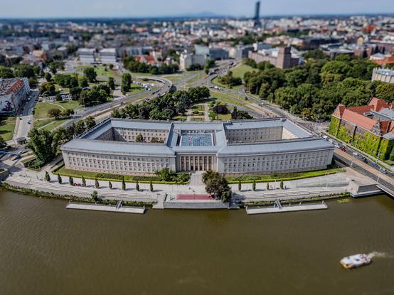 Aerial view of a U-shaped government building with a river in the foreground and a cityscape in the background.

Widok z lotu ptaka na budynek rządowy w kształcie litery U z rzeką na pierwszym planie i pejzażem miasta w tle.