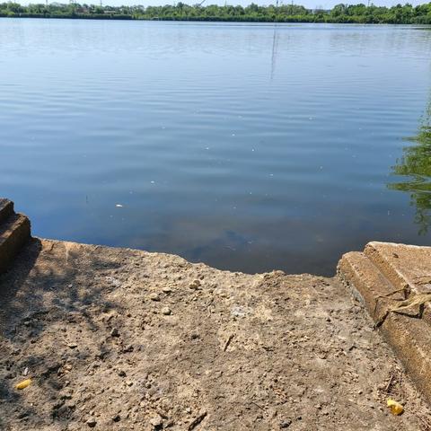 Photograph of a damaged, concrete structure out into open water with trees and other greenery seen in the background.
