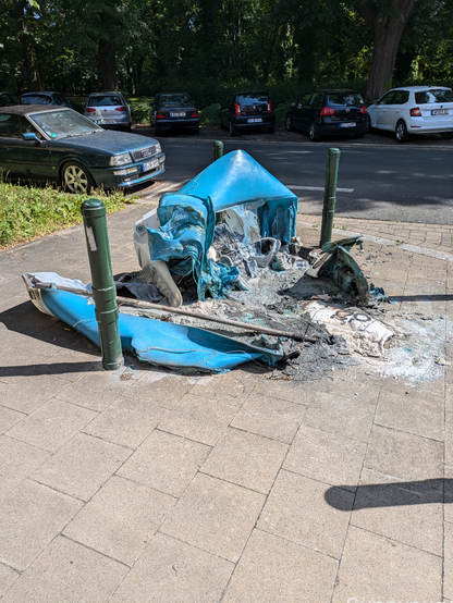 Ein zerschmolzenes, da verbranntes Dixiklo. Auf dem Gehweg.