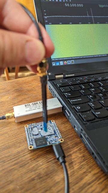 Abstrahlende Frequenzen einer Platine werden mittels E-Sonde und Software Defined Radio gemessen. Ein Laptop zeigt ein Frequenzspektrum und Wasserfalldiagramm an.