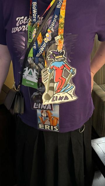 Photo of me from the neck down showing a few convention badges. Some say Lina showing my raccoon fursona, one says Eris showing my shark.