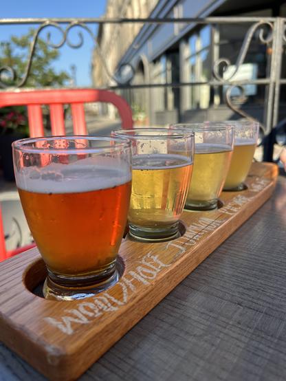 A flight of beer(s?) on a table outside on a patio.