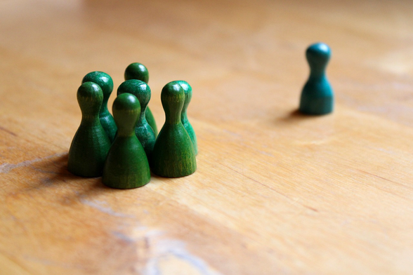 Sieben grüne Spielfiguren stehen eng zusammne, eine steht einzeln abseits.