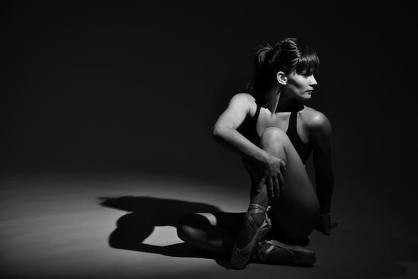 Black haired woman dancing in a grey studio