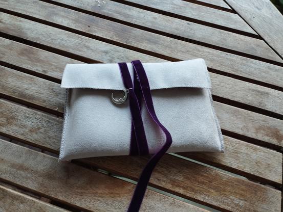 Pochette en tissu blanc écru fermée d'un cordon violet agrémenté d'une lune argentée. Cette pochette contient le jeu de rôle "magie de minuit", c'est à dire un jeu de tarot et un livret explicatif, pour jouer un coven de sorcières.