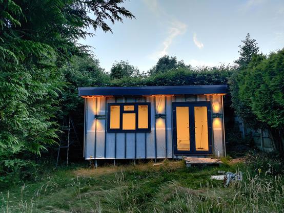 garden office with lights glowing from the windows and doors and also 3 external up/down lighters giving a nice warm glow to the front.